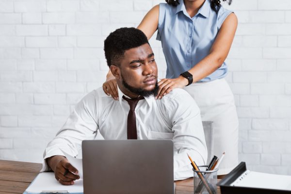 Lady boss sexually molesting her attractive male subordinate, putting hands on his shoulders at company office. Young businesswoman harassing her handsome coworker at workplace