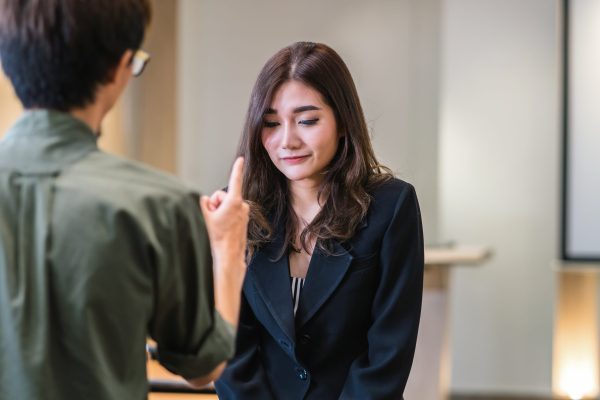 Reaw view of Furious boss scolding asian young businesswoman in formal suit by point to her face in modern office, Business mistake and punish concept