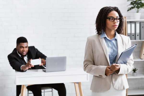 Sexual molestation at workplace. Perverted black guy taking photo of his female coworker without her consent at company office, blank space. Gender discrimination and career concept