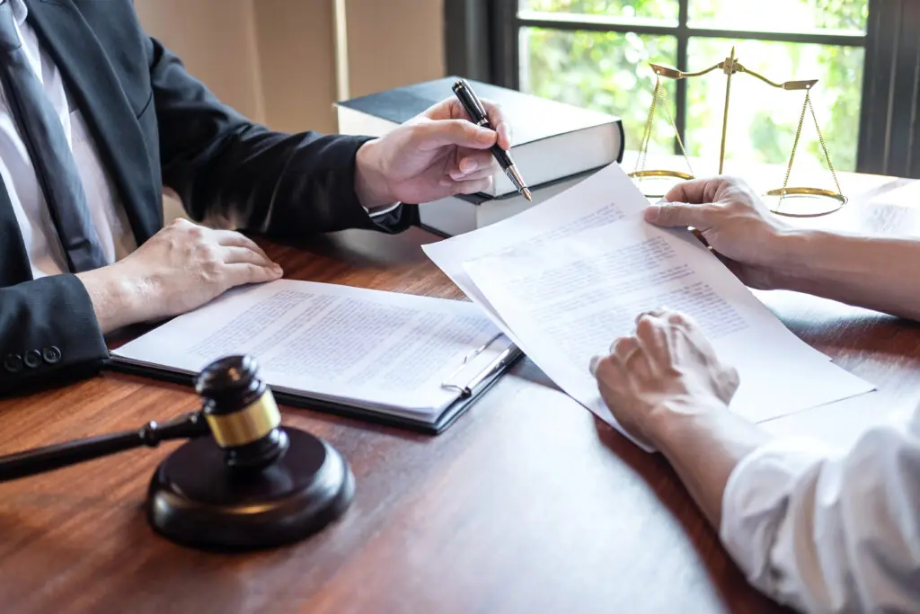 Person signing legal paperwork beside a gavel.