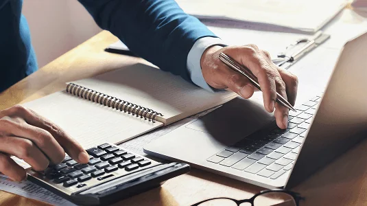 Close-up of a person writing notes beside a laptop.