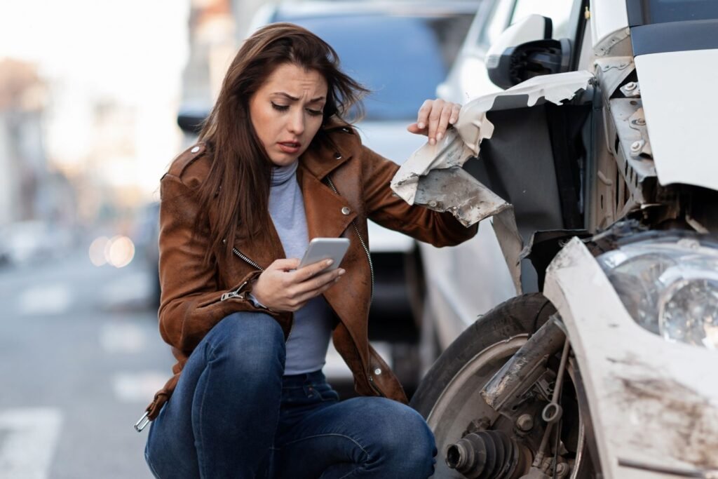Driver checking her phone next to a damaged car after a Los Angeles car accident, highlighting the importance of documenting the crash and seeking legal help